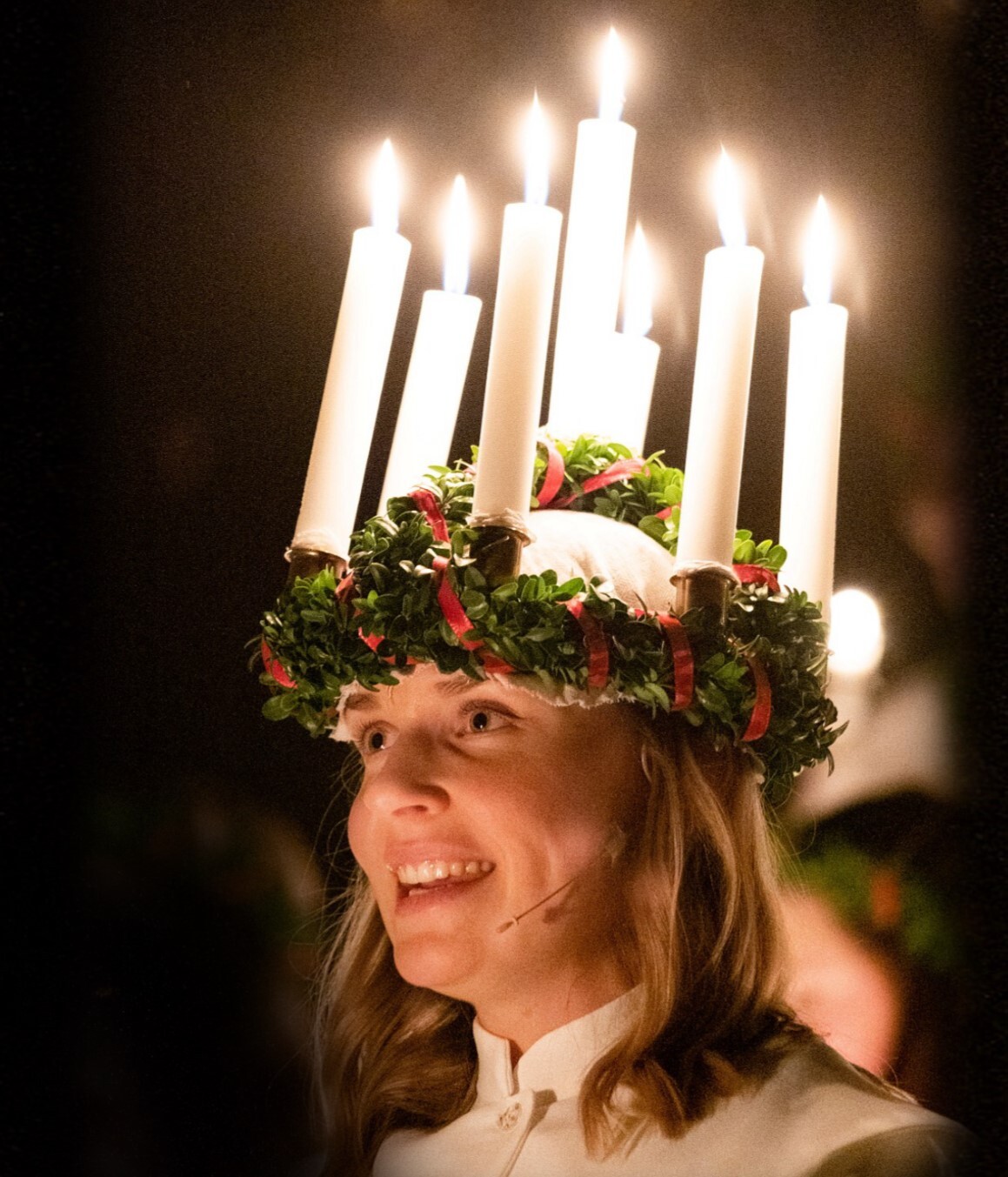 Eine singende Frau in weißem Kleid trägt einen Kranz mit leuchtenden Kerzen, Foto: rechtefrei