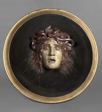 Rundes Medaillon mit Medusa-Kopf aus Bronze auf dunklem Hintergrund mit goldenem Rahmen