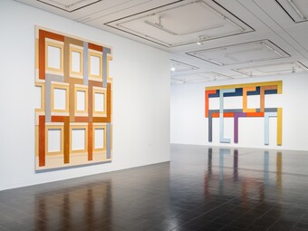 Galerie mit beleuchteten, orangefarben gerahmten Wandobjekten und dunklem Boden