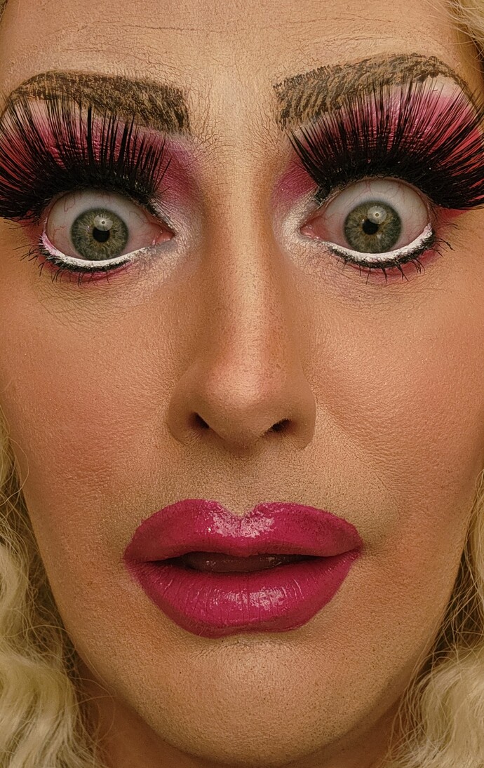 Drag mit dramatischem Make-up, langen künstlichen Wimpern und pinkem Lippenstift