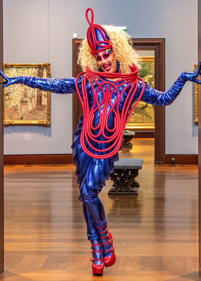 Farbenfroh gkleidete Drag Queen in Tanzpose in einer Kunstgalerie