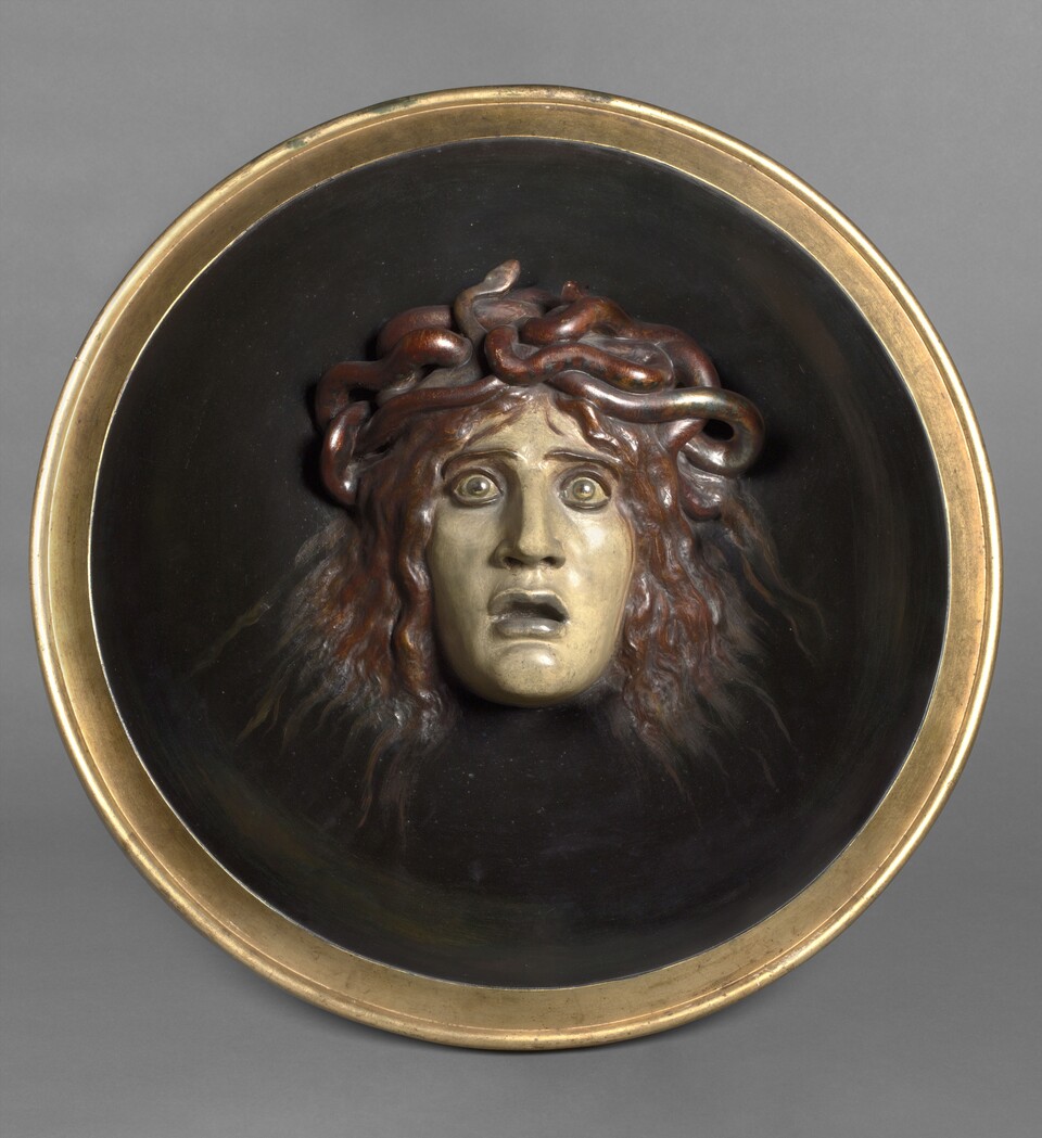 Rundes Medaillon mit Medusa-Kopf aus Bronze auf dunklem Hintergrund mit goldenem Rahmen