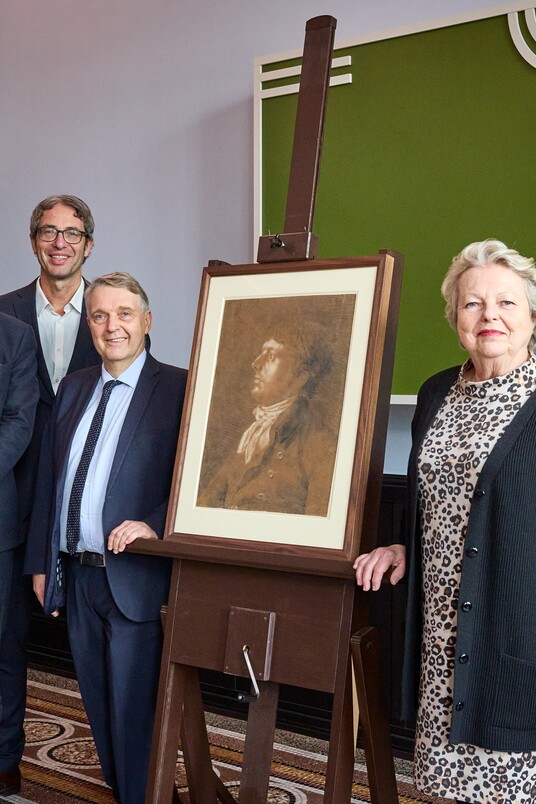 Fünf Personen stehen neben einem gerahmten Philipp Otto Runge Zeichnung auf einer Staffelei bei einer formellen Veranstaltung.