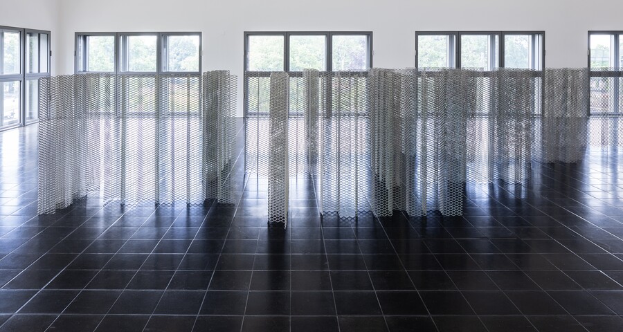 Raum mit großen Fenstern, dunklem Holzboden und zaunartigem Kunstwerk