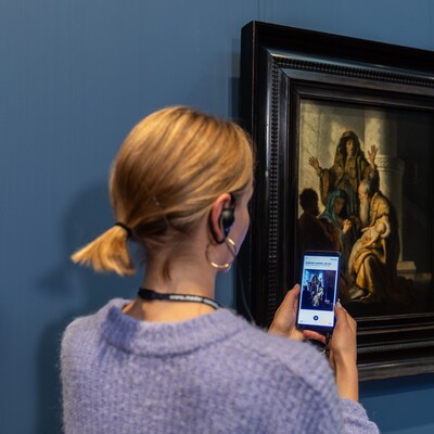 Eine Frau mit Handy und Kopfhörern vor dem Gemälde von Rembrandt Harmensz. van Rijn (1606–1669)