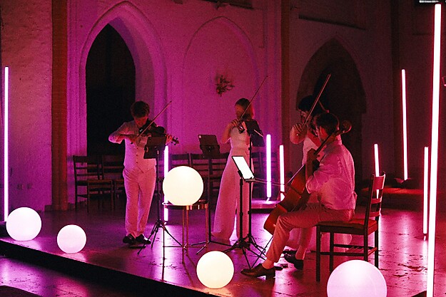 Musiker auf einer Bühne mit pinker Beleuchtung und weißen Kugelleuchten im Vordergrund